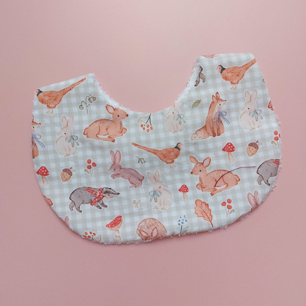 Baby bib with a light green and white background. Features woodland animal motifs, mushrooms and leaves throughout.