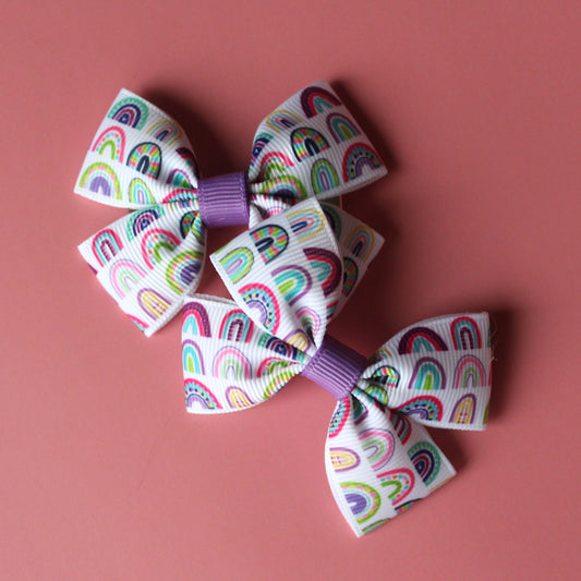 Pair of bow hair clips with bold purple rainbow pattern.