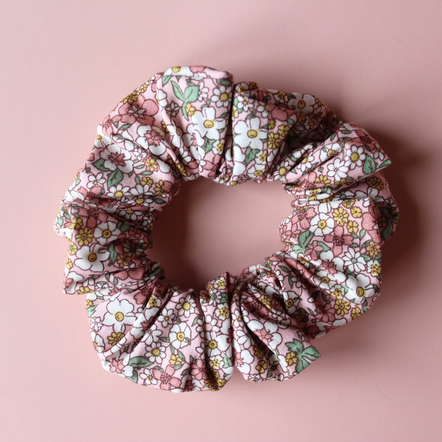 Floral patterned hair scrunchie in pink with white, yellow and green all over pattern.