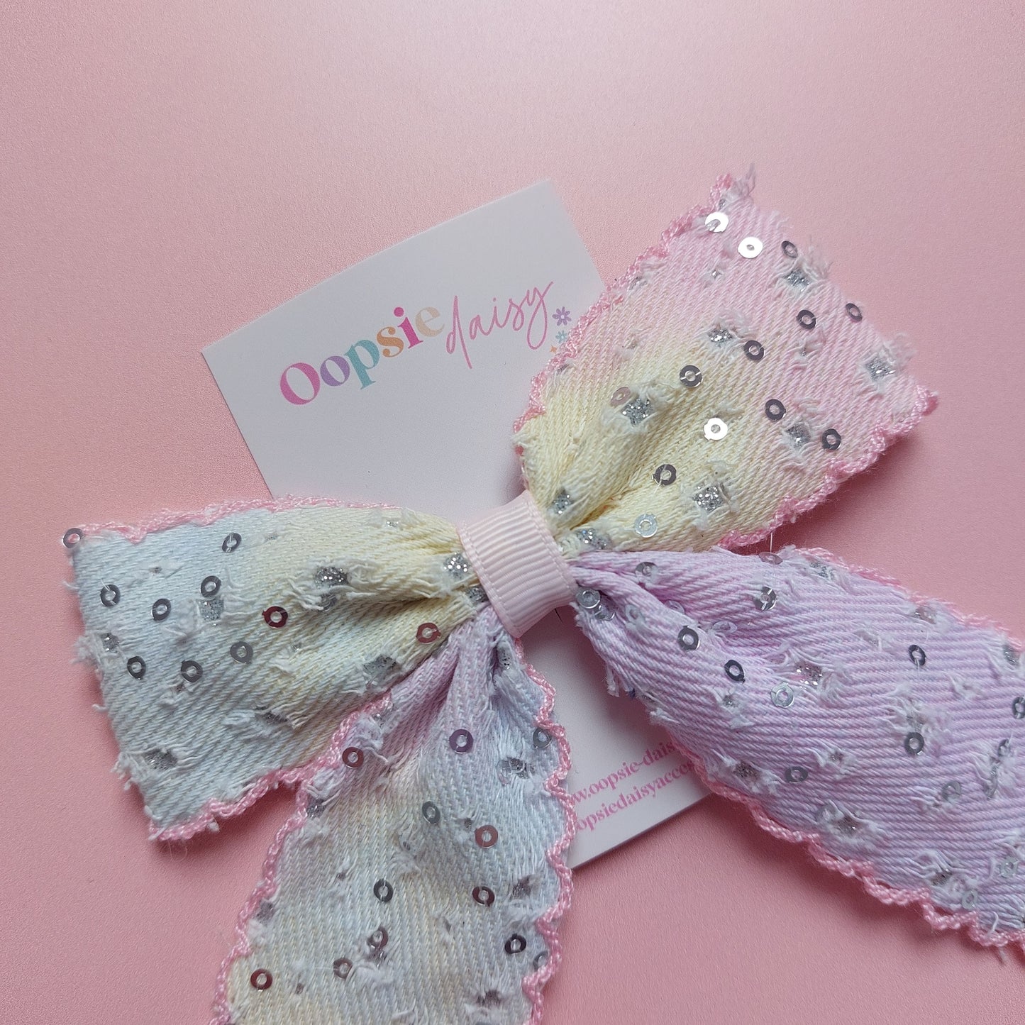 A pastel rainbow gradient hair bow with sequins, displayed on a pink background 