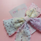 A pastel hair bow with sequined details, displayed on a pink background 