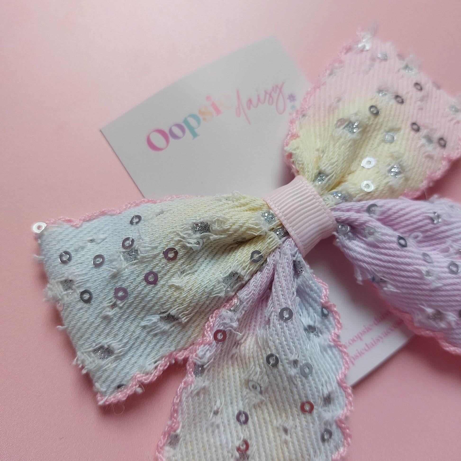 A pastel hair bow with sequined details, displayed on a pink background 