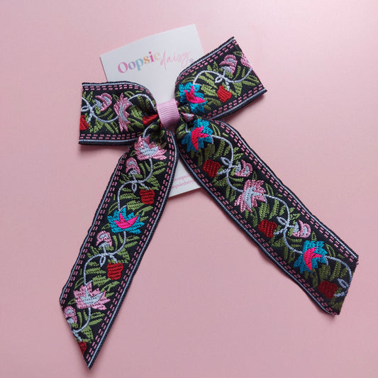A decorative embroidered hair bow with a black base and colourful floral embroidery in pink, blue, green, and red.