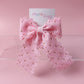 A pink ribbon bow with scalloped edges and small gold polka dots, attached to a white card printed with the brand name 'Oopsie Daisy', set against a solid pink background.