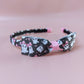 A black alice headband with bow with a pattern of white ghosts wearing pink bows. 