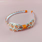 Alice style bow headband with a pattern of orange pumpkins on a white background. 