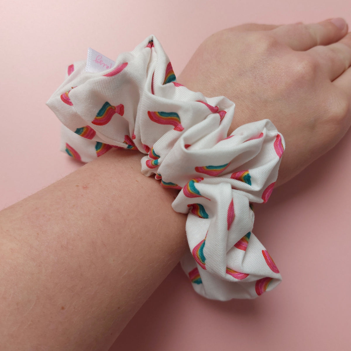 Oversized hair scrunchie with colourful rainbows scattered on an off-white background worn on a wrist