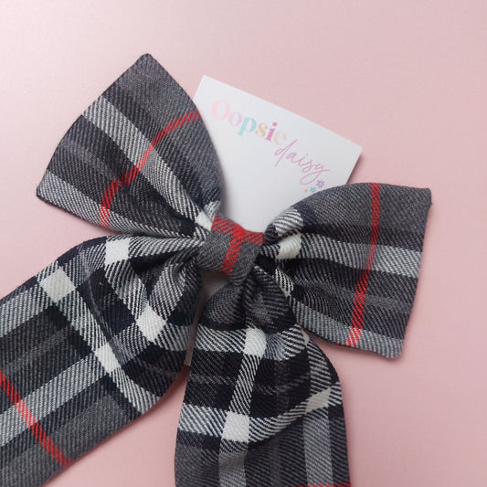 A long tailed hair bow made from grey, white and red tartan fabric. 