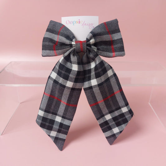 A long tailed hair bow made from grey, white and red tartan fabric. 
