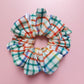 Multicolour check oversized hair scrunchie. Neutral background with red, blue, yellow and green checks. 