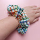 Multicolour check oversized hair scrunchie. Neutral background with red, blue, yellow and green checks. 