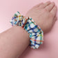 Hair scrunchie with multicolour checked pattern. Off-white background with red, blue, green and yellow checks. 