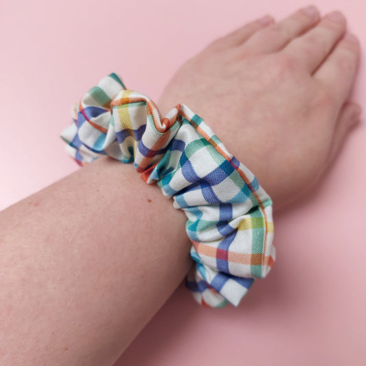 Hair scrunchie with multicolour checked pattern. Off-white background with red, blue, green and yellow checks. 