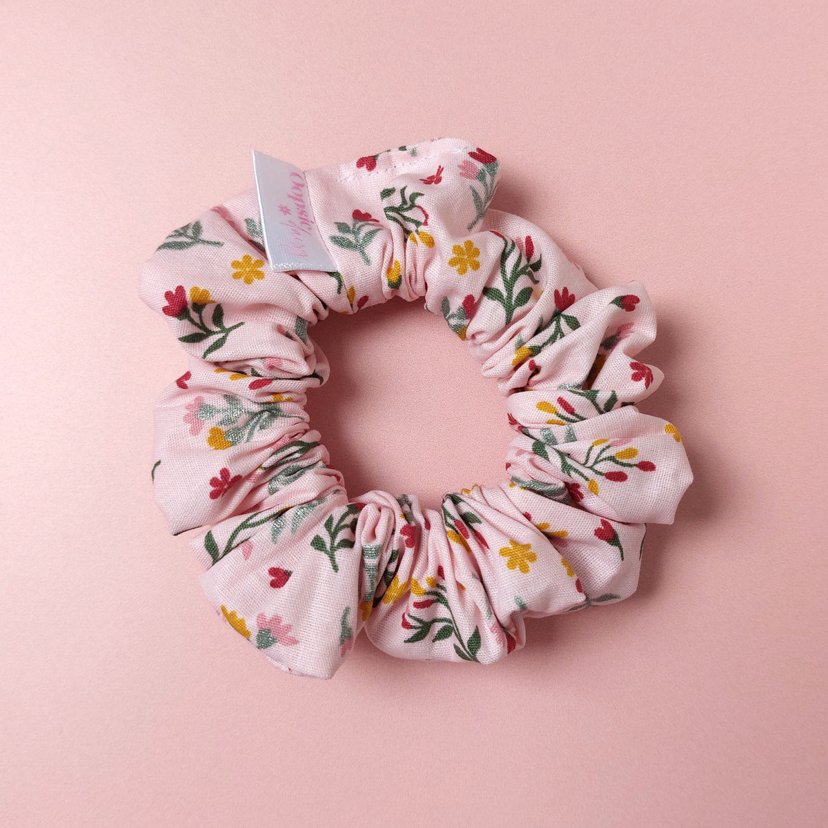 Pink hair scrunchie with botanical pattern. Red, yellow and yellow flowers scattered with green leaves. 