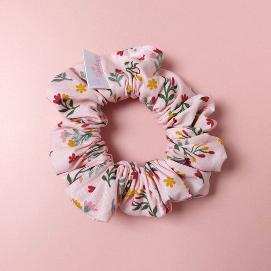 Pink hair scrunchie with botanical pattern. Red, yellow and yellow flowers scattered with green leaves. 