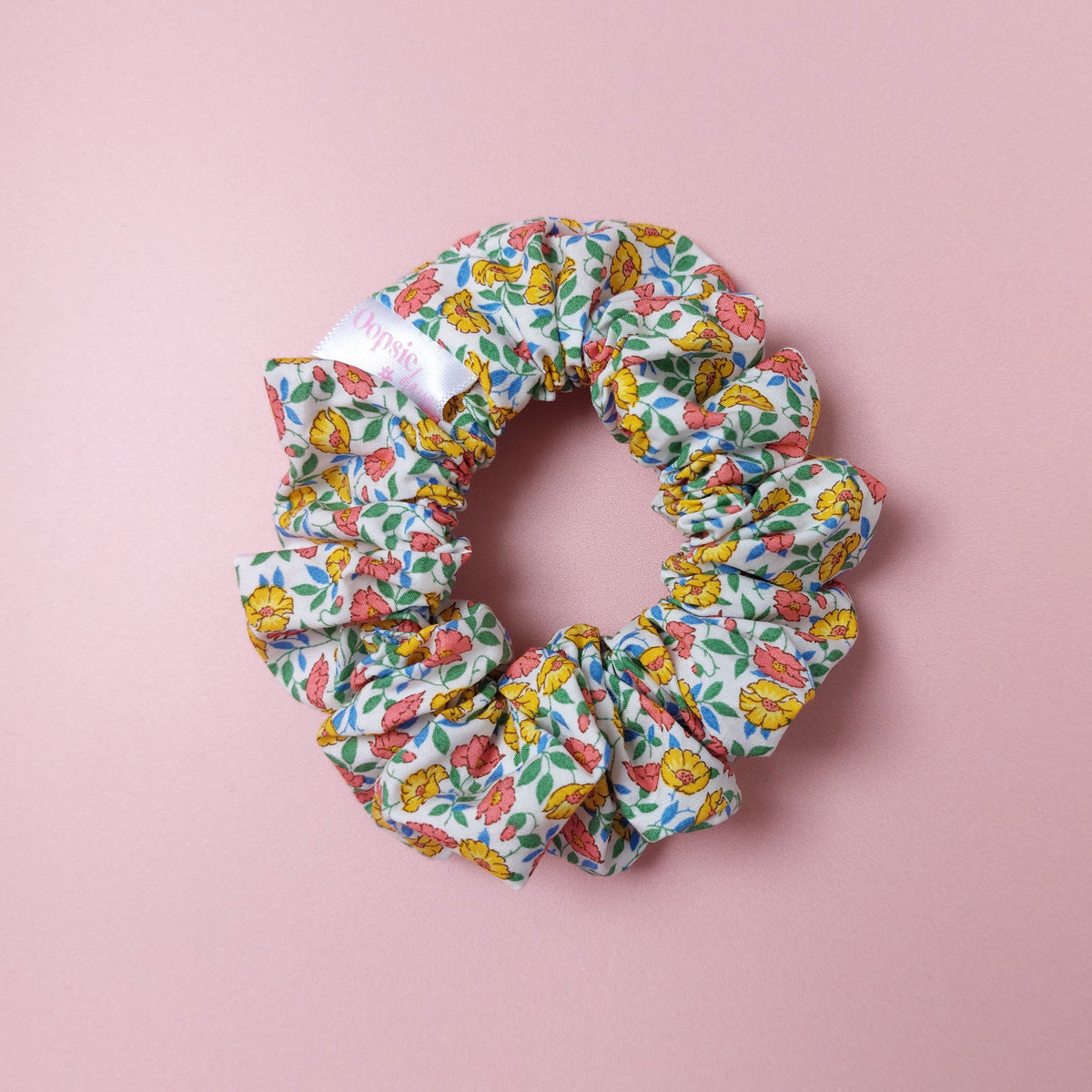 Floral hair scrunchie. Off-white background with ditsy pattern of yellow and coral flowers with blue and green leaves.