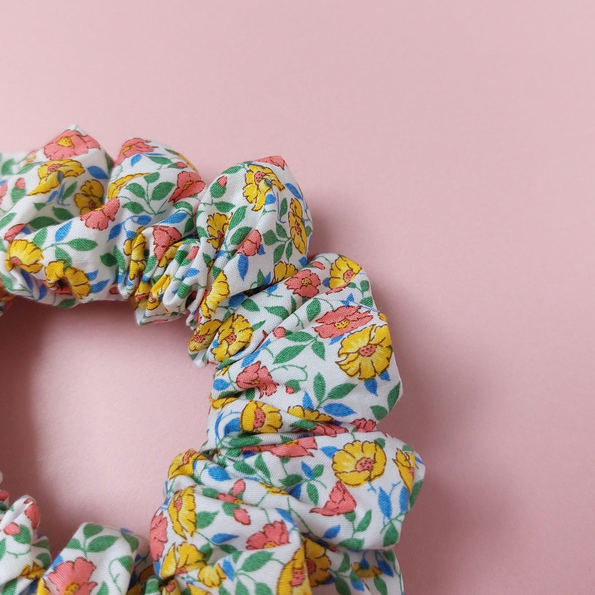 Floral hair scrunchie. Off-white background with ditsy pattern of yellow and coral flowers with blue and green leaves.