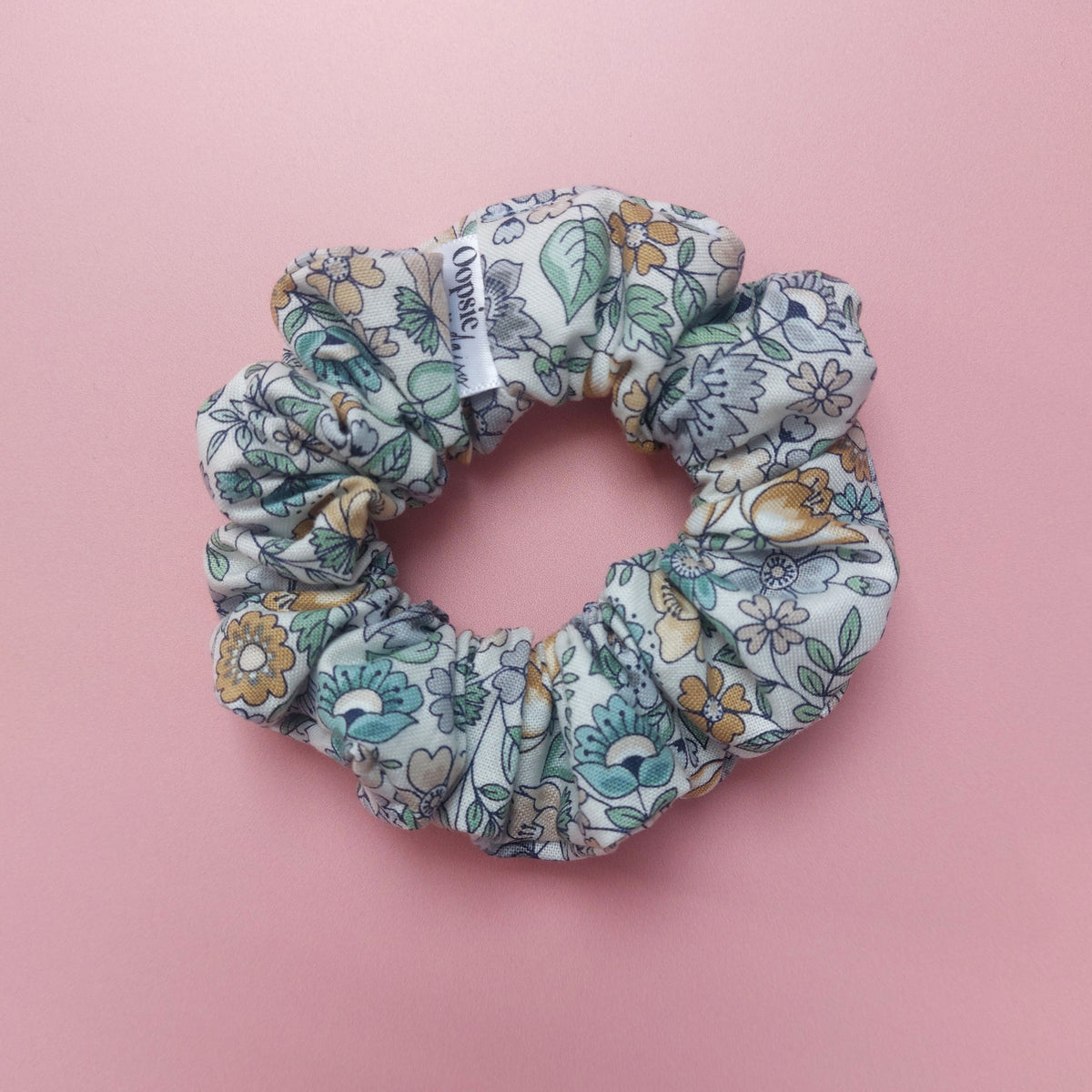 Muted toned hair scrunchie. With a floral pattern in shades of green and golden tones.