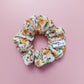Corduroy scrunchie in autumnal leave and floral pattern. With orange, green, yellow and red colours. 