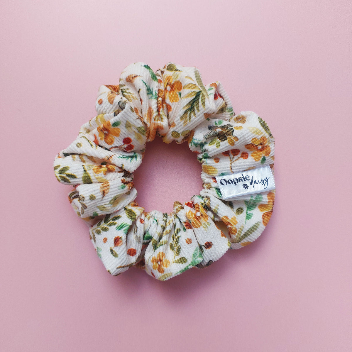 Corduroy scrunchie in autumnal leave and floral pattern. With orange, green, yellow and red colours. 