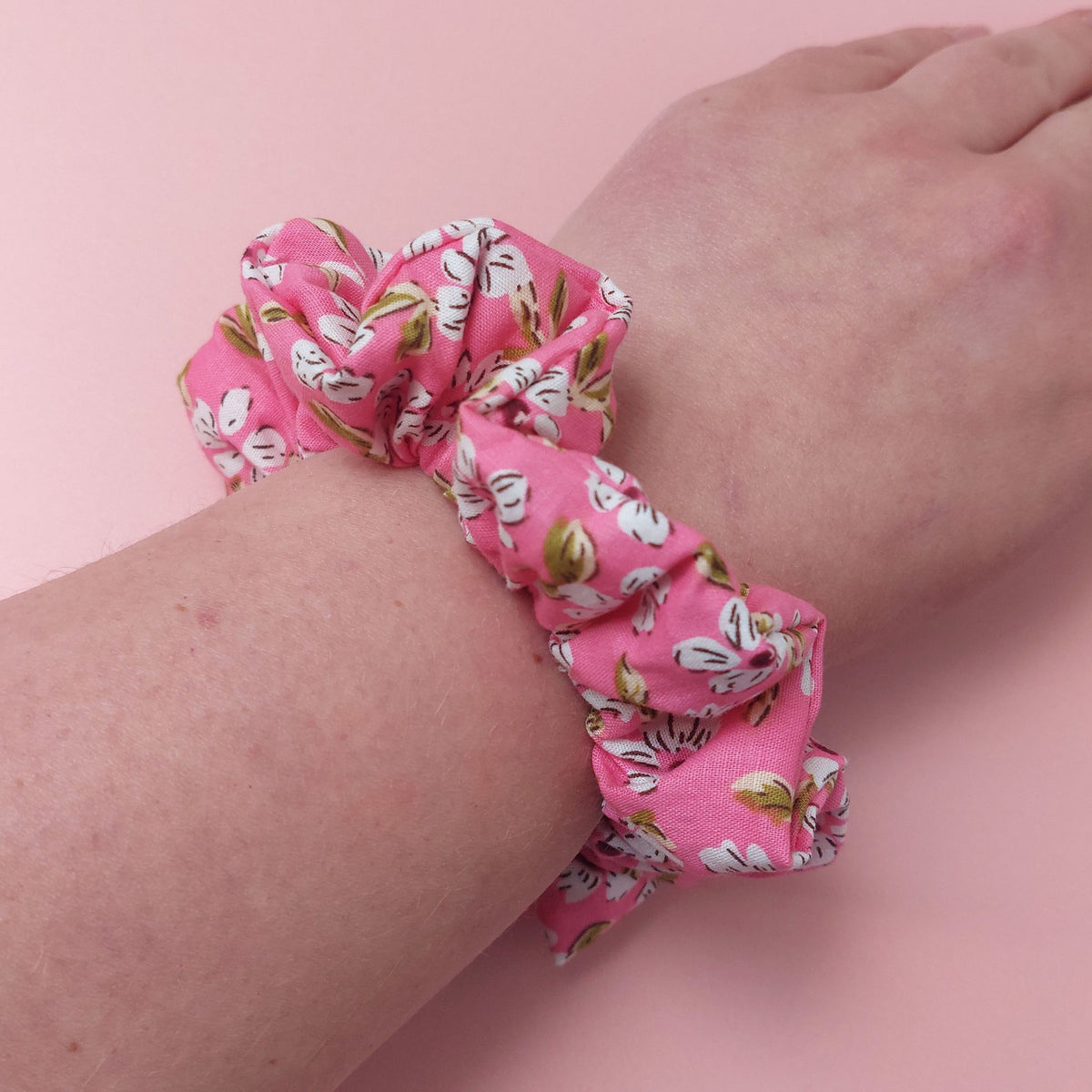Bright pink scrunchie with white flowers and green leaves. 
