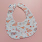Baby bib with a light green and white background. Features woodland animal motifs, mushrooms and leaves throughout. 