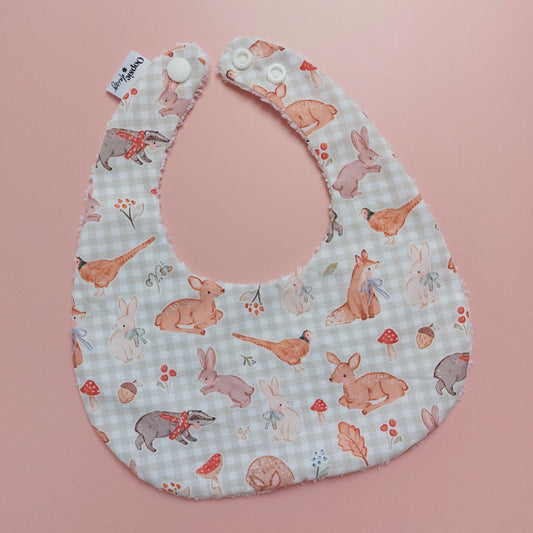 Baby bib with a light green and white background. Features woodland animal motifs, mushrooms and leaves throughout. 