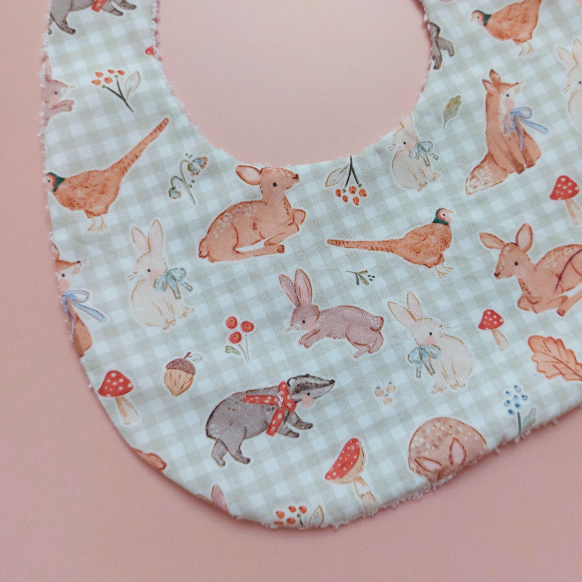 Baby bib with a light green and white background. Features woodland animal motifs, mushrooms and leaves throughout. 