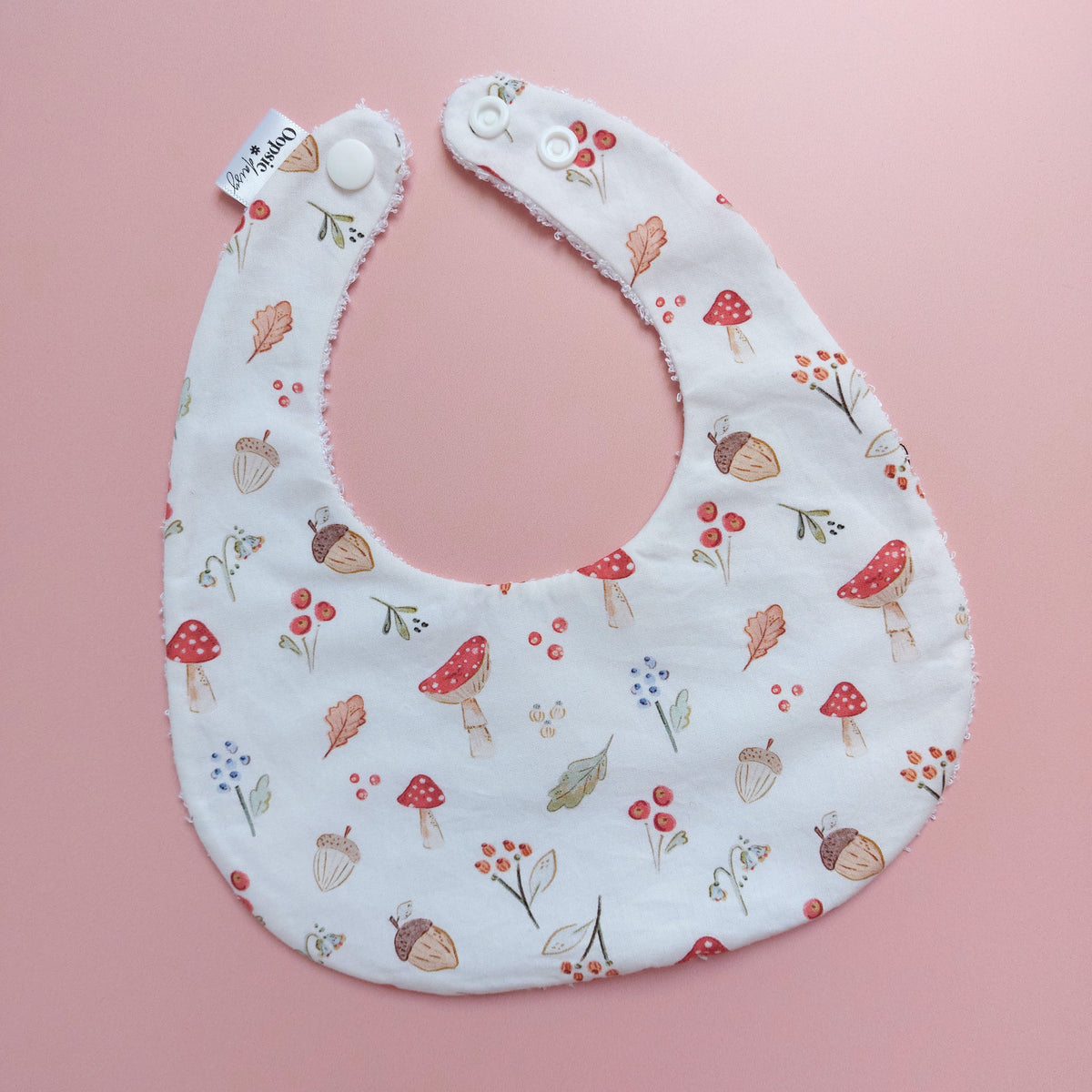 White round shaped baby bib with autumnal pattern of mushrooms, acorns, leaves and autumn flowers. 