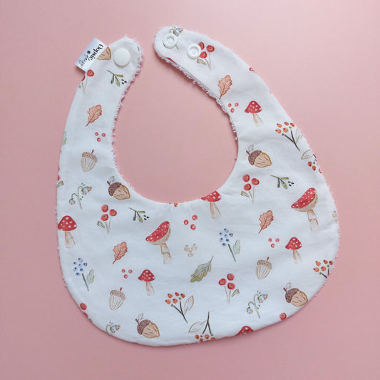 White round shaped baby bib with autumnal pattern of mushrooms, acorns, leaves and autumn flowers. 