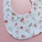 White round shaped baby bib with autumnal pattern of mushrooms, acorns, leaves and autumn flowers. 