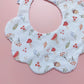 Scallop edged baby bib in white with autumnal pattern. Featuring mushrooms, acorns, leaves and autumnal flowers. 