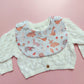 Baby bib with a light green and white background. Features woodland animal motifs, mushrooms and leaves throughout. 