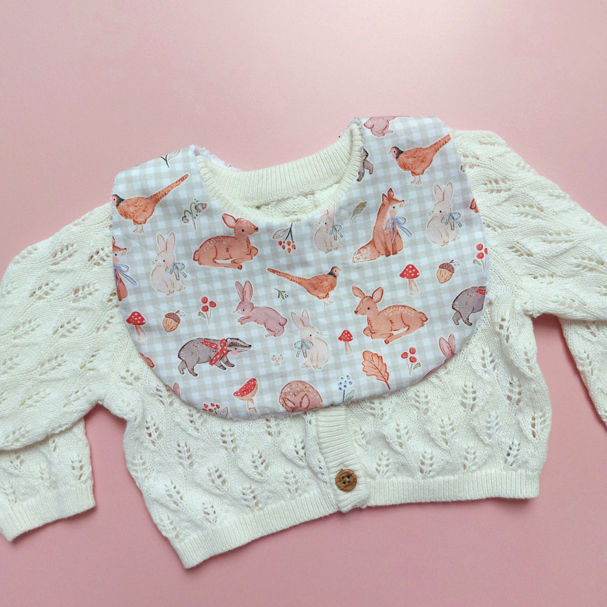 Baby bib with a light green and white background. Features woodland animal motifs, mushrooms and leaves throughout. 