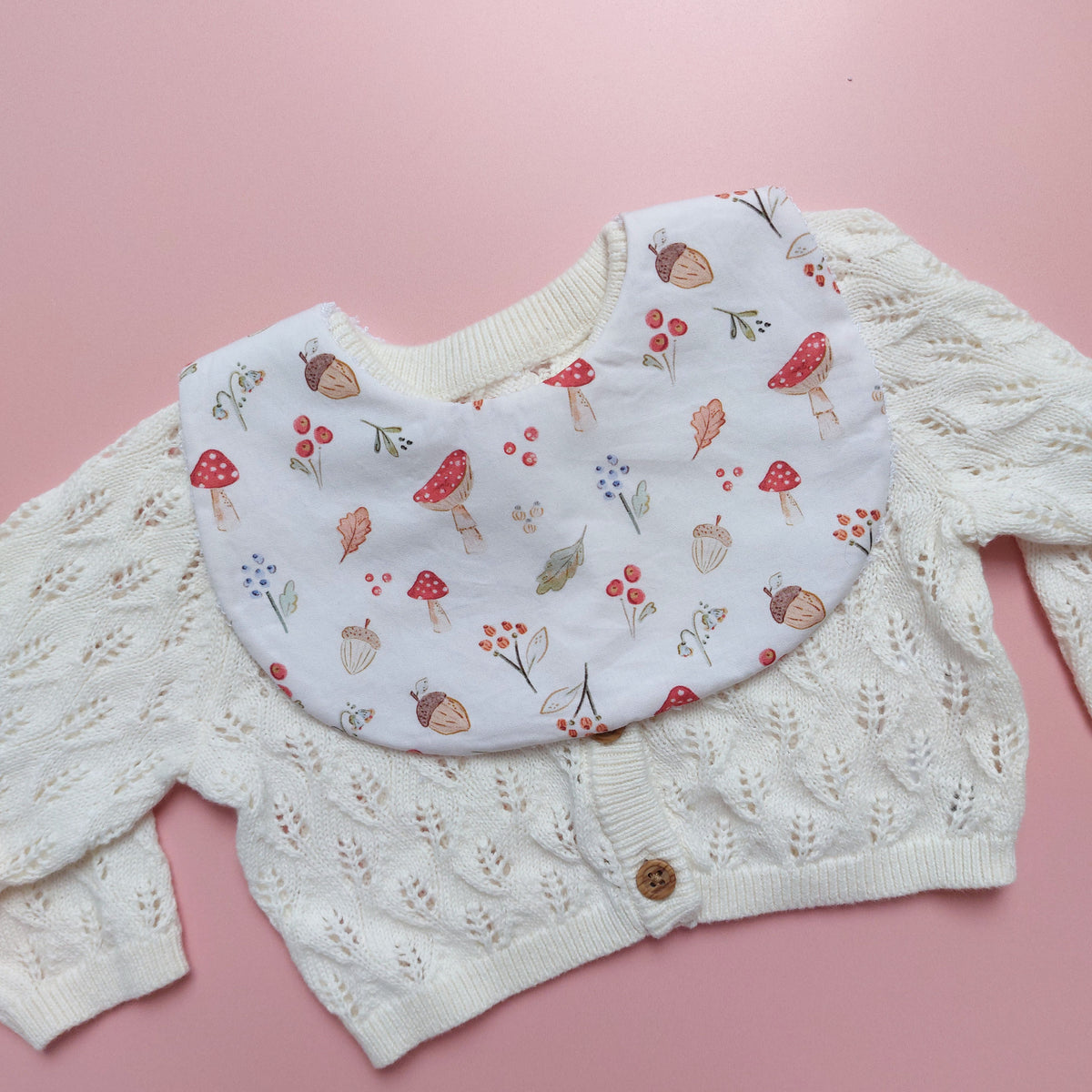 White round shaped baby bib with autumnal pattern of mushrooms, acorns, leaves and autumn flowers. 