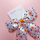 Satin hair bow in pink with orange flowers, pumpkins, white ghosts and black stars. 