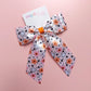 Satin hair bow in pink with orange flowers, pumpkins, white ghosts and black stars. 