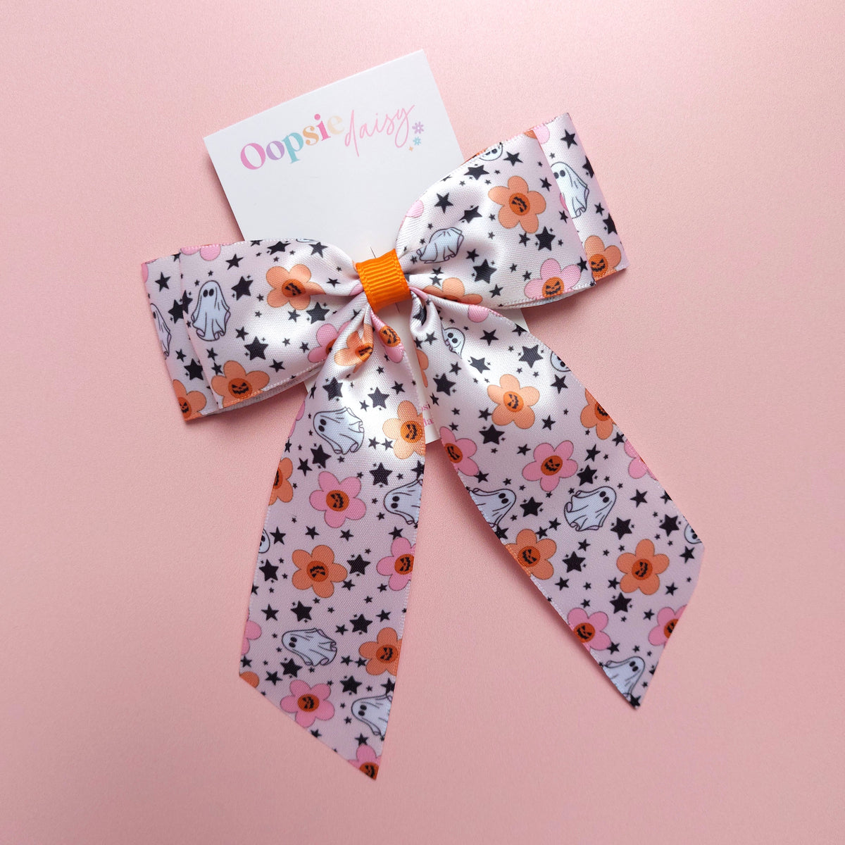 Satin hair bow in pink with orange flowers, pumpkins, white ghosts and black stars. 