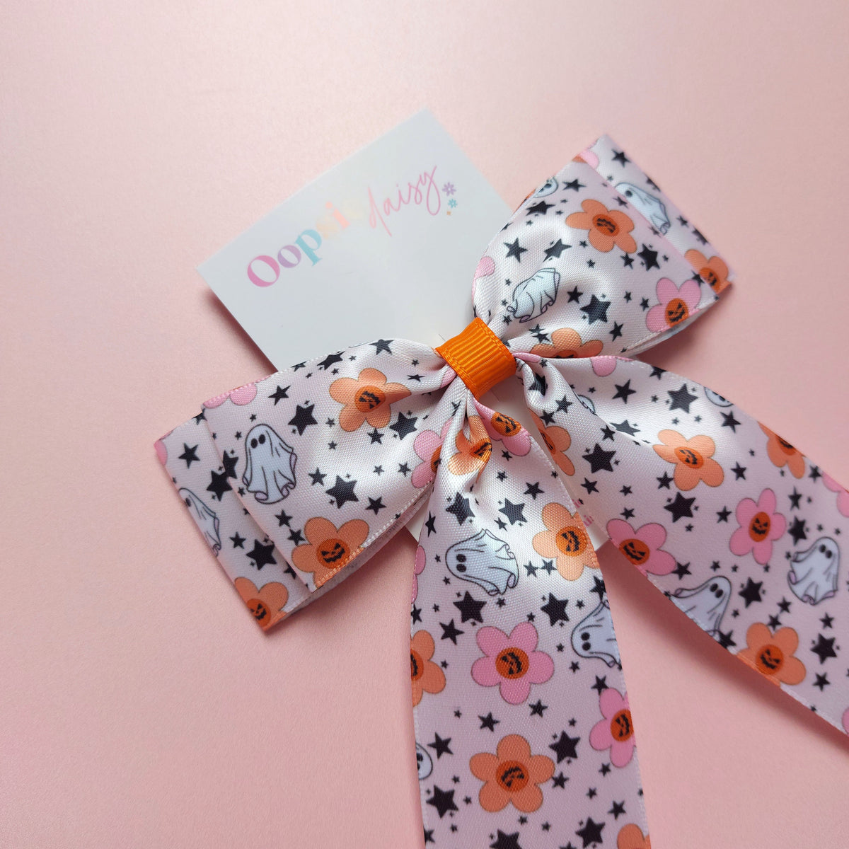 Satin hair bow in pink with orange flowers, pumpkins, white ghosts and black stars. 