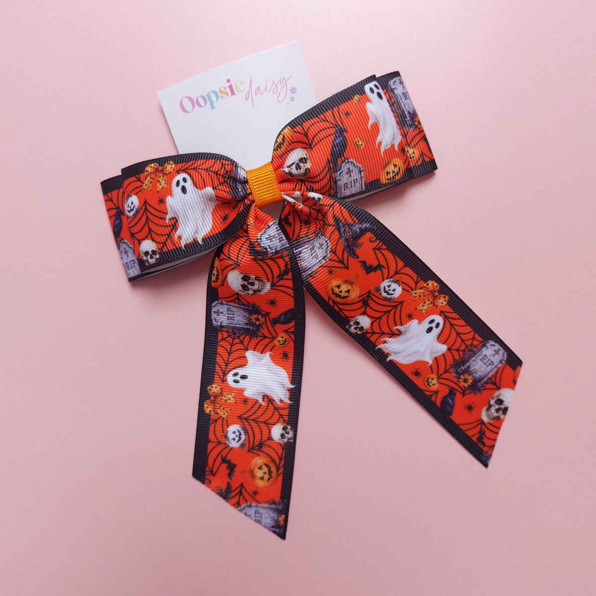 A Halloween-themed grosgrain ribbon bow with a orange, white and black pattern featuring ghosts, skulls, pumpkins, and tombstones.