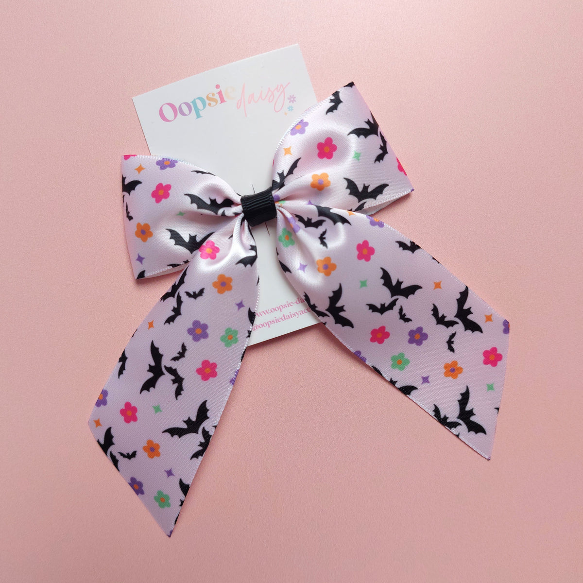 A satin hair bow with a bat pattern accented with small colourful flowers.