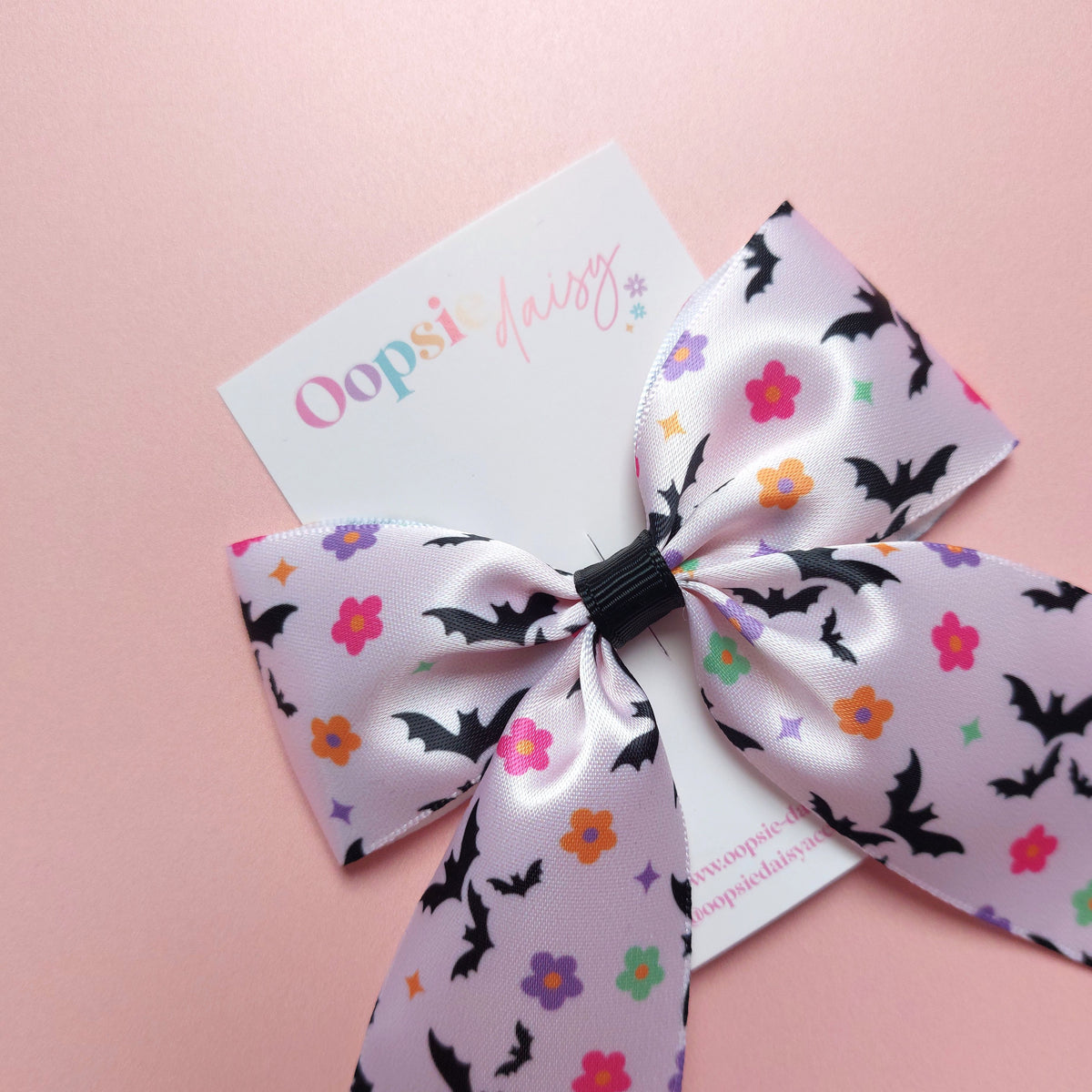 A satin hair bow with a bat pattern accented with small colourful flowers.