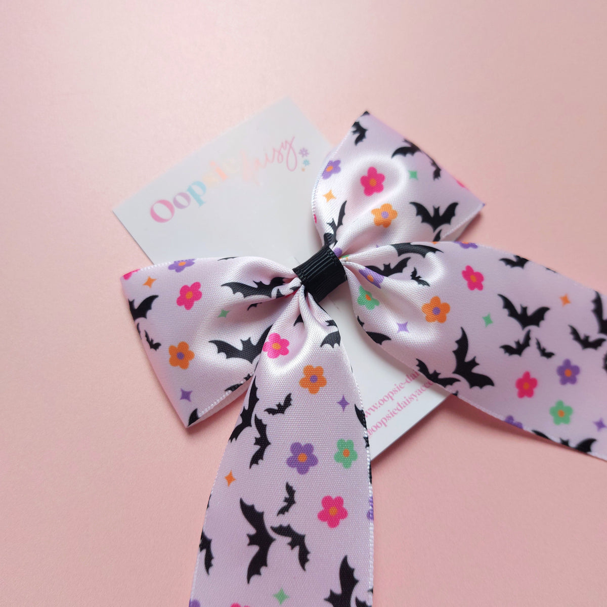 A satin hair bow with a bat pattern accented with small colourful flowers.