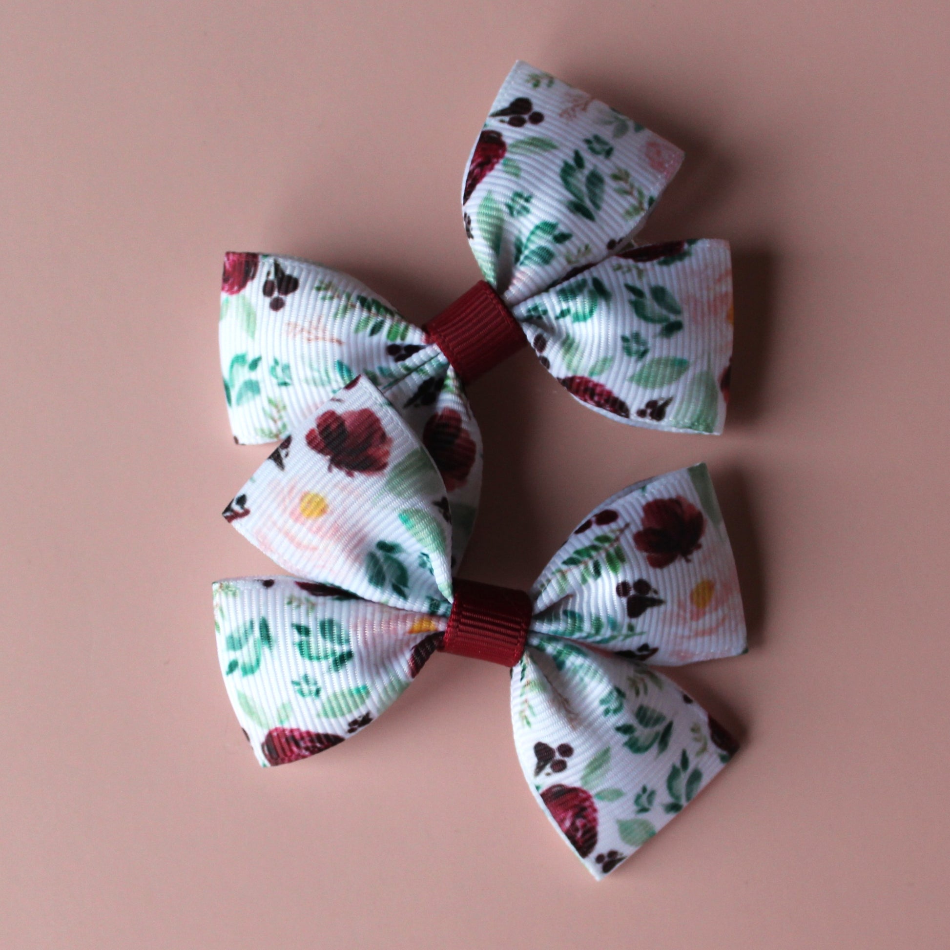 Two bow hair clips with flower pattern in burgundy and pink with green leaves