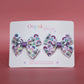 Pair of bow hair clips with bold purple rainbow pattern. 