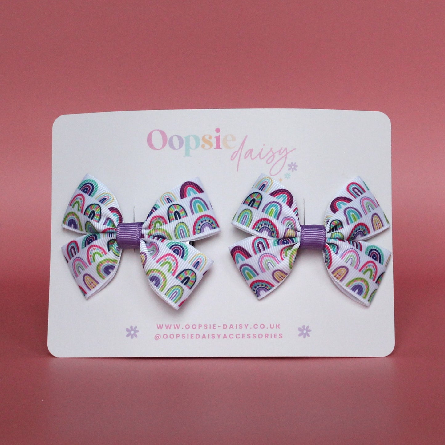 Pair of bow hair clips with bold purple rainbow pattern. 