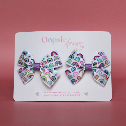 Pair of bow hair clips with bold purple rainbow pattern. 