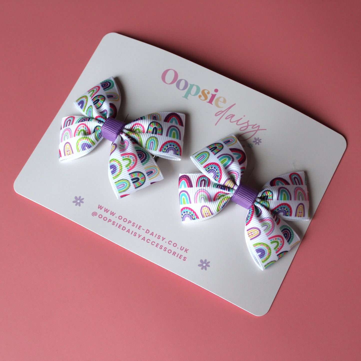 Pair of bow hair clips with bold purple rainbow pattern. 