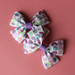 Pair of bow hair clips with bold purple rainbow pattern. 