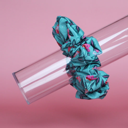 A teal scrunchie with a floral pattern of pink and dark green leaves. 